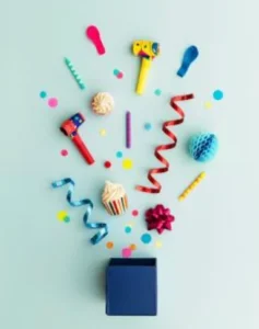 A blue gift box surrounded by colorful party decorations, including confetti, streamers, noise makers, and a cupcake, arranged in a playful burst against a light blue background.