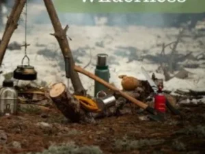 A collection of camping tools and supplies arranged on the forest floor, including a kettle, a thermos, an axe, and a multi-tool, surrounded by natural foliage and tree branches.
