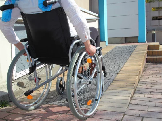 A person in a wheelchair navigating a ramp made of brick and stone outside a building, with a focus on the wheels of the wheelchair.
