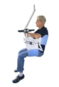 A person seated in a mobile lifting device, designed for assistance, with adjustable arm supports and a harness, shown against a white background.