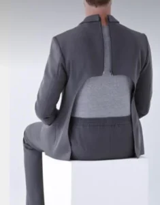 A person sitting on a white cube, wearing a gray suit with a unique back opening. The person is facing away, revealing a gray undershirt beneath the suit jacket.