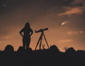 A silhouette of a person standing near a telescope, gazing at a comet in the night sky, with stars visible in the background. This image highlights the interest in astronomy and celestial events.