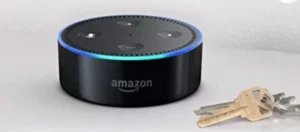 A black Amazon Echo Dot smart speaker with a blue LED ring, placed on a surface next to a set of keys.