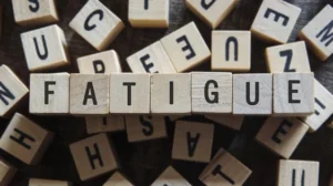 Wooden letter tiles arranged on a surface, spelling the word "FATIGUE" in the center, surrounded by other letter tiles. The image represents the concept of SCI Fatigue.