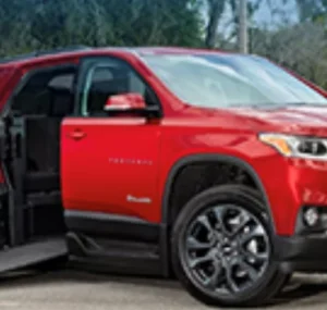 A red Chevrolet Traverse SUV parked with the driver's side door open, showing a spacious interior and a lowered ramp for accessibility.