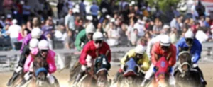 A group of jockeys in colorful attire riding thoroughbred horses during a race at Assiniboia Downs. Spectators are visible in the background, watching the event in a lively atmosphere.