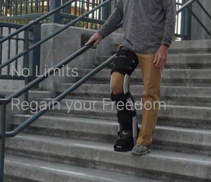 A person wearing a knee brace walks down outdoor stairs. The individual is dressed in a long-sleeve shirt and khaki pants, using a handrail for support. Text on the image reads 'No Limits' and 'Regain your Freedom'.