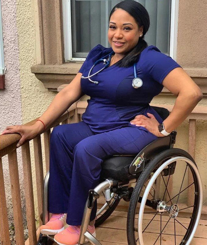 A healthcare professional wearing a blue uniform and a stethoscope, seated in a wheelchair on a balcony. The setting features light-colored walls and a window in the background.