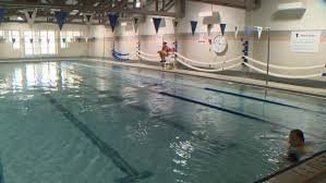 An indoor swimming pool at the YMCA downtown, featuring lanes marked by ropes, with a swimmer in the water and lifeguards present on the poolside.