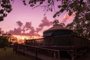 Show a photo of a eight sided yurt with an accessible ramp and a beautiful purple and orange sunset