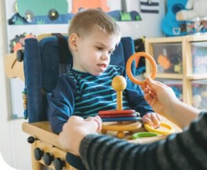 Picture show the young disabled boy approximately six years old sitting in a chair, well-being rehabilitated with devices colourful