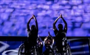 The Rollettes a female dance group that are in wheelchairs perform on stage with purplelighting in the background
