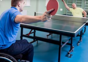 Two persons in wheelchairs playing a game of ping-pong, wearing in a blue shirt or a yellow shirt