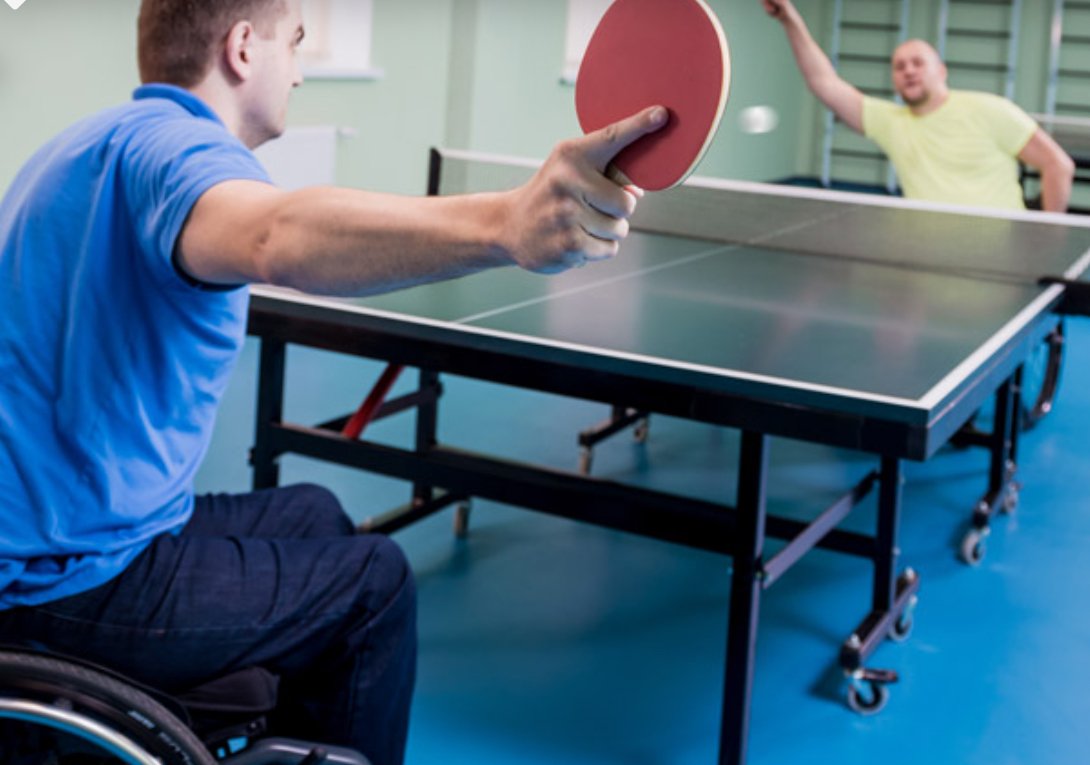 Two persons in wheelchairs playing a game of ping-pong, wearing in a blue shirt or a yellow shirt