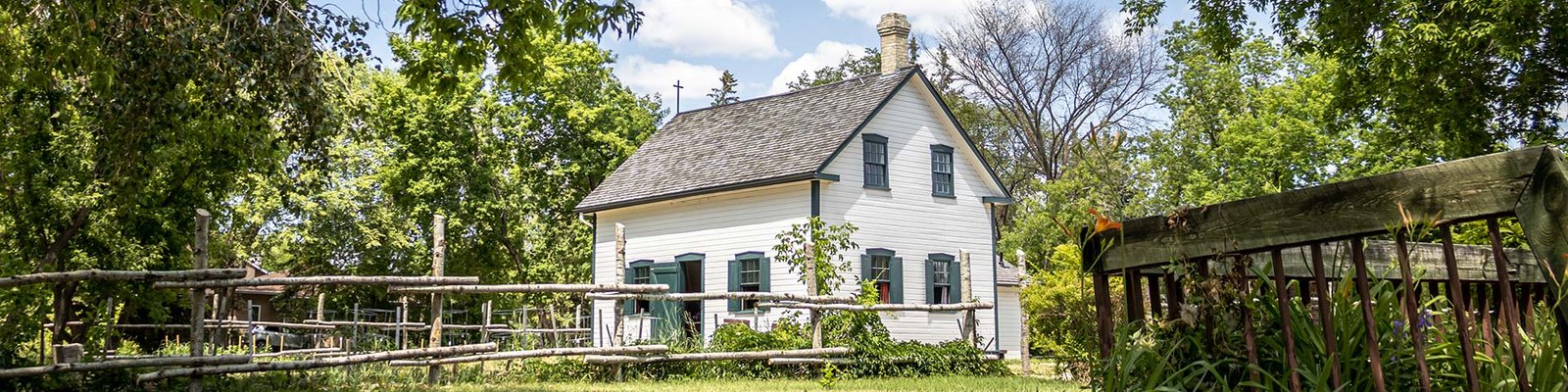 Historic former home of Louis riel is white with green trim with a fence in the foreground