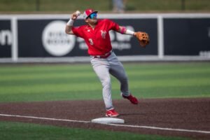 Winnipeg gold eyes player wearing a red top and a red hat and gray pants at shortstop position is throwing the ball after fuelling it