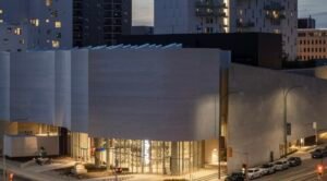 A street view of the Winnipeg Art Gallery and Inuit art centre at night time beautiful bright lights in the corner entrances and the white brick with that background of the other city buildings