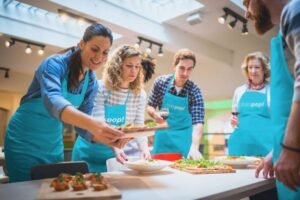 Men and women with their class pop teal aprons are enjoying setting up a feast on a table