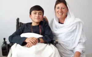 Boy from Afghanistan poses for picture sitting with his mother