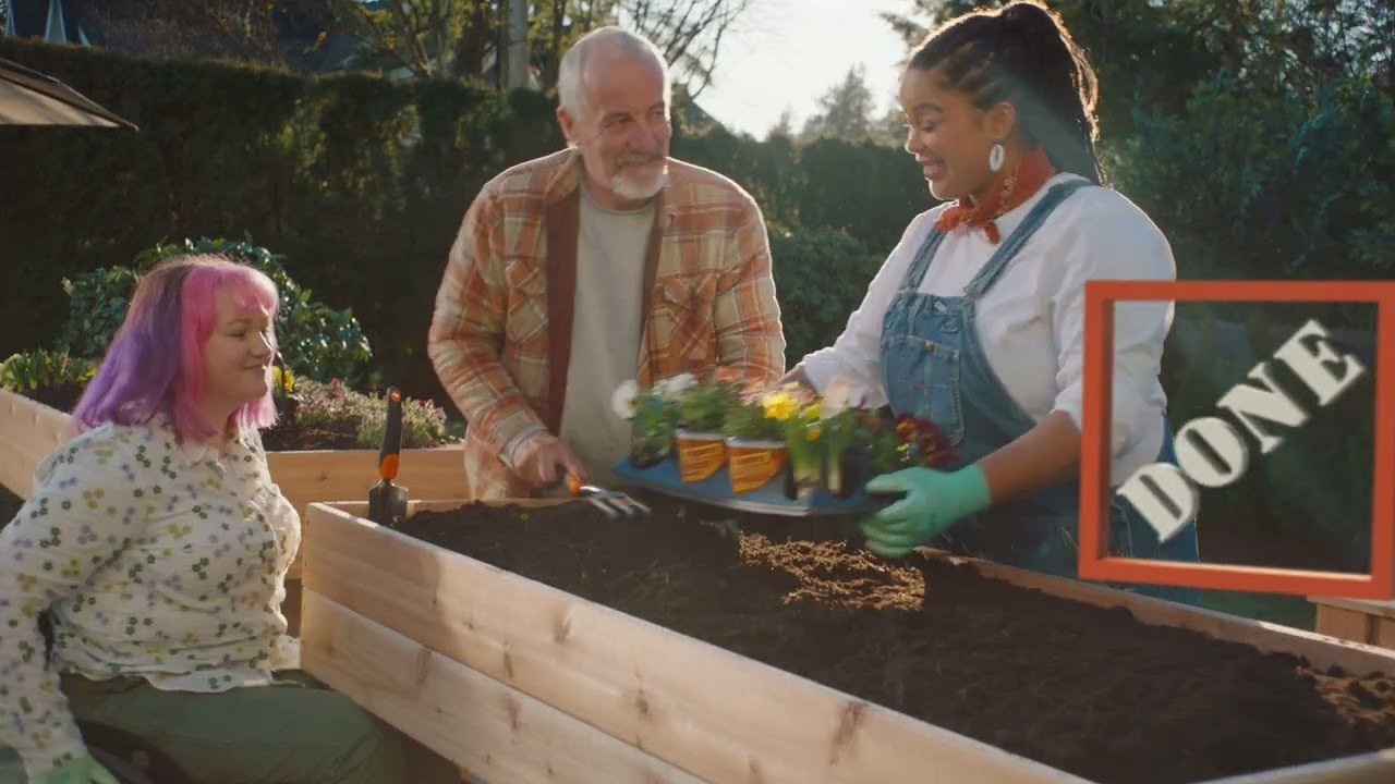 A man and a woman dressed in some overalls and work shirt or standing above a raised garden bed that they have built. The woman in a wheelchair is on the other side
