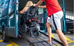 A person in a wheelchair being assisted up a ramp into a green conversion van. The person helping is wearing a red shirt and shorts, ensuring eco medical accessibility.