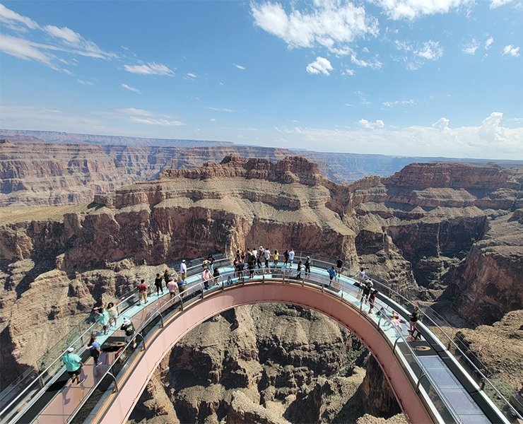 Tourists visiting the Grand Canyon Skywalk, a glass bridge extending over the canyon, with stunning rock formations visible below. The scene highlights Beautiful Accessible Viewpoints in the World.
