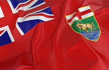 A close-up of the flag of Manitoba, Canada, featuring a red background with the Union Jack in the top left corner and the provincial coat of arms on the right side.