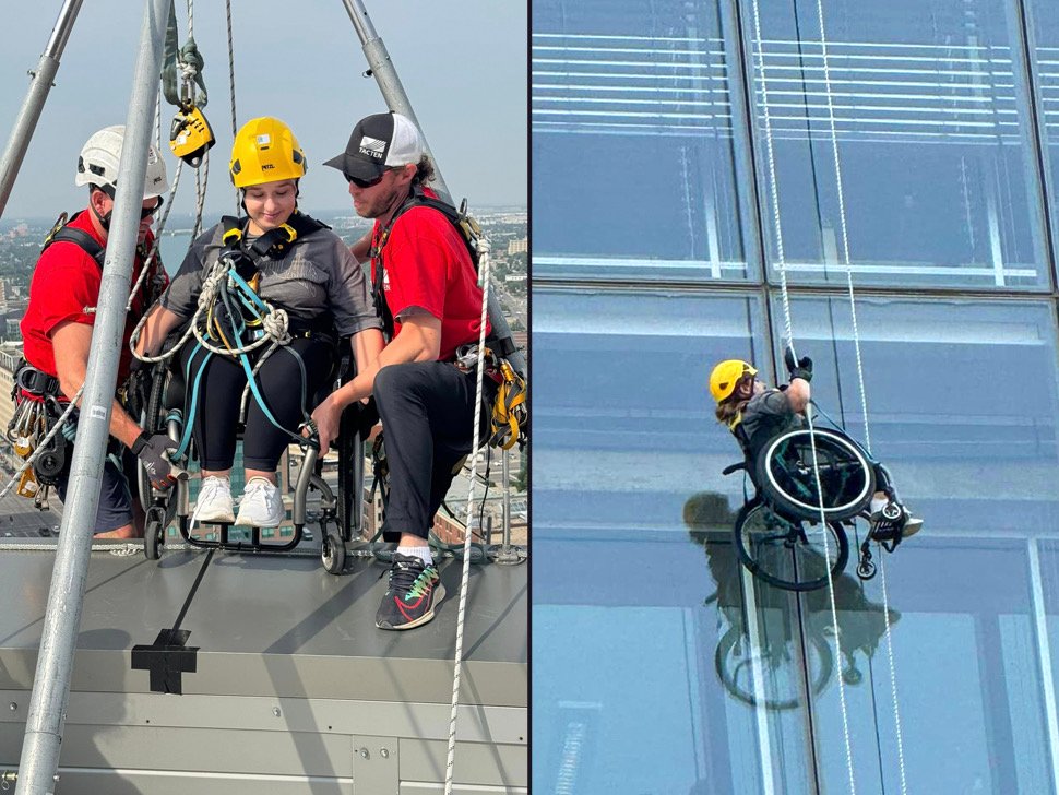 Two men helping a woman in a wheelchair as she gears up to rappel down a building.