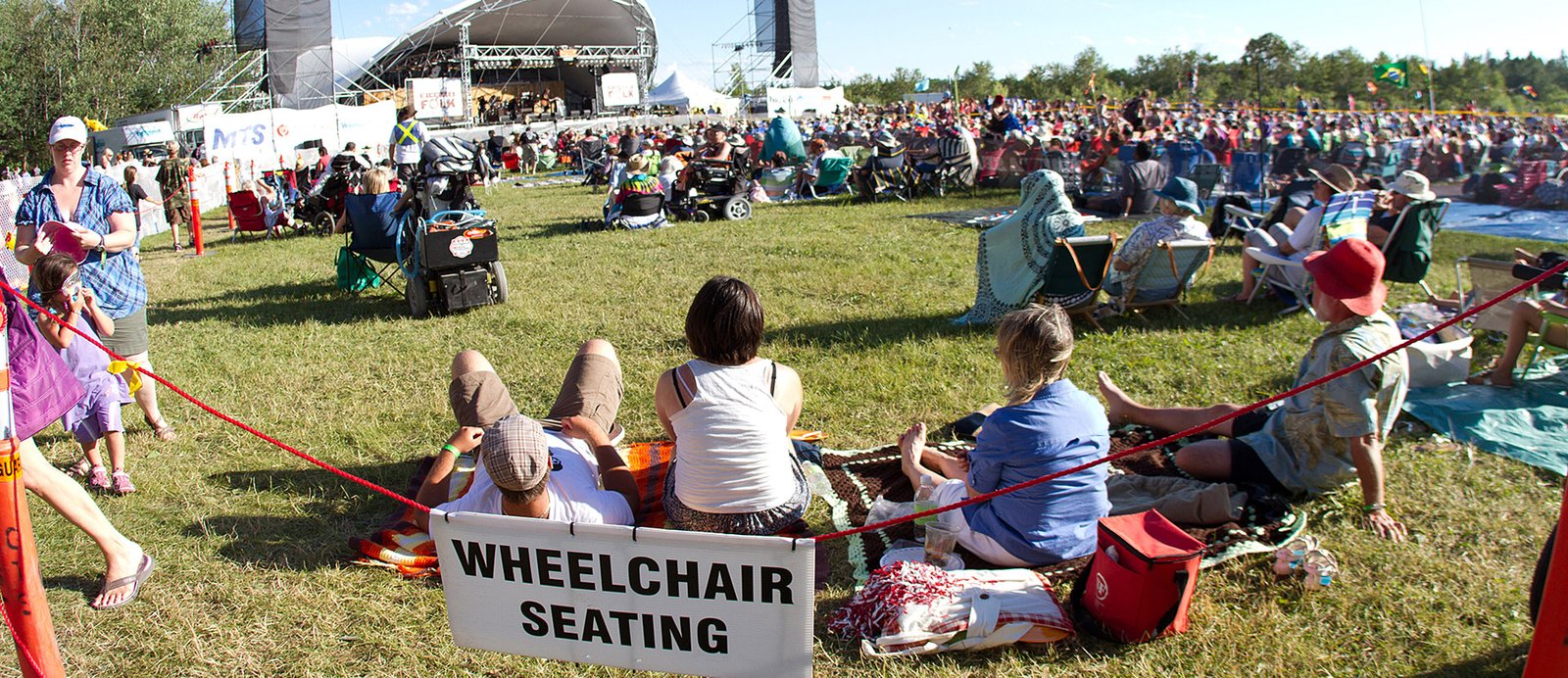 A group of people sitting a grass attending an outdoor seminar for people with disabilities.