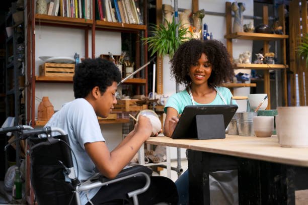 A woman and a boy in wheelchairs are seated at a table, engaged in conversation.