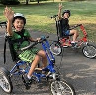 Two young boys cycling together on a paved road, enjoying a sunny day outdoors.