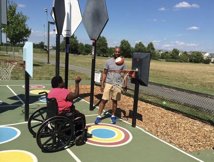 A woman in a wheelchair and a boy play basketball together on an outdoor court, showcasing teamwork and inclusivity.