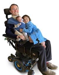 A man and two children are smiling while seated in a wheelchair, showcasing a moment of togetherness and joy.