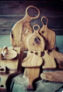 A collection of wooden cutting boards and serving platters displayed on a rustic surface, showcasing various shapes and sizes, with visible wood grain patterns.