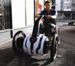 A man operating a small electric wheelchair, traveling along a pathway in a bustling city environment.
