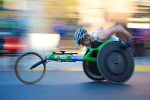 Disabled athlete is hunched over and pushing the rear wheels of his three wheeler racing cycle, and the image is blurred in the background indicating he’s going fast