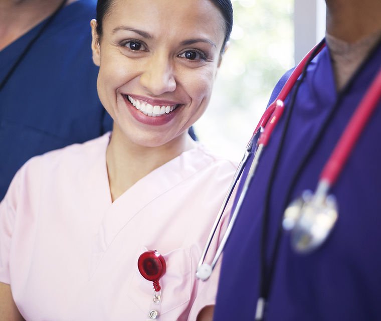 Amongst other hospital, staff dressed in blue, a nurse female, dressed in pink with a stethoscope around her neck.
