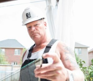 Photo of Mike Holmes just overalls on a white heart hat, looking at the camera on side of our home