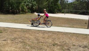 Woman is cycling riding an adaptive bike with a disabled child is sitting in the front of it in a park trail