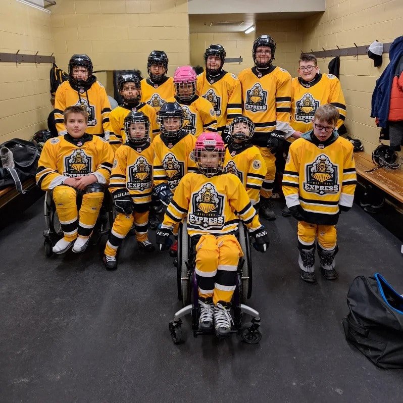 Young group of teenagers, dressed in team, Manitoba, yellow, and black colours somehow their sleds and somehow have their sticks posing for our team picture