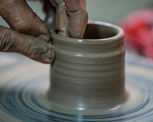 Shows a hand smoothing a rotating piece of clay into a cup.