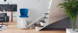 Photo shows a staircase in the Home outfitted with a chairlift was blue and white, and the walls are white and the stairs are wood trim