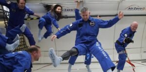 Four astronauts floating in a simulation space environment with a disabled male astronaut in the forefront floating in the air spread eagle