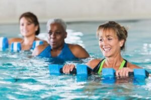 The senior aged women are in the swimming pool with floating dumbbells doing exercises