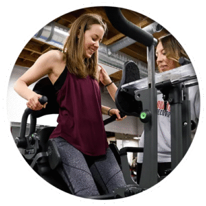 A young lady client is being assisted by a therapist on a arm exercise machine at the wellness clinic