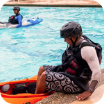 Young adult wearing a helmet and a life jacket being assisted getting into a kayak in the city of Winnipeg swimming pool practice class
