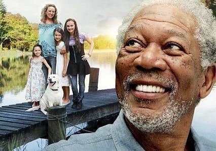 Morgan Freeman a black actor is on a big part of the screen looking up into the sky. Behind him is a family with a mother and three daughters and a dog sitting on a dock on a lake with trees in the background.