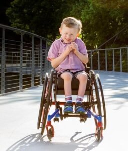 Picture of young boy being happy to sit in a wheelchair on a pathway with the sun shining