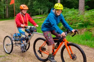 Disabled young man sits in rear section of adaptive bike cycled by woman in blue