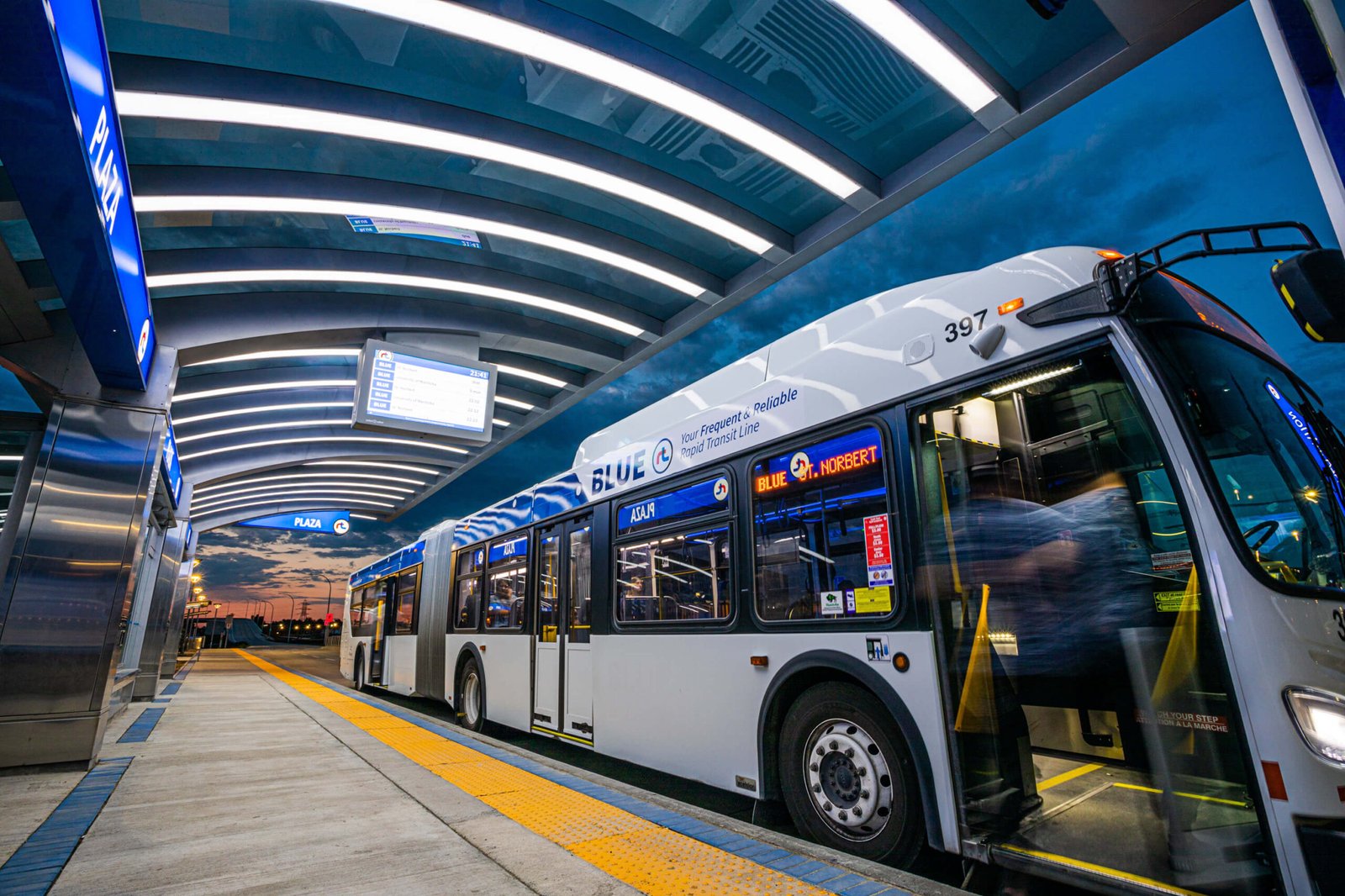A large welder bus garage has a double length, transit bus, white, and blue FaceTime Adam angle towards the front